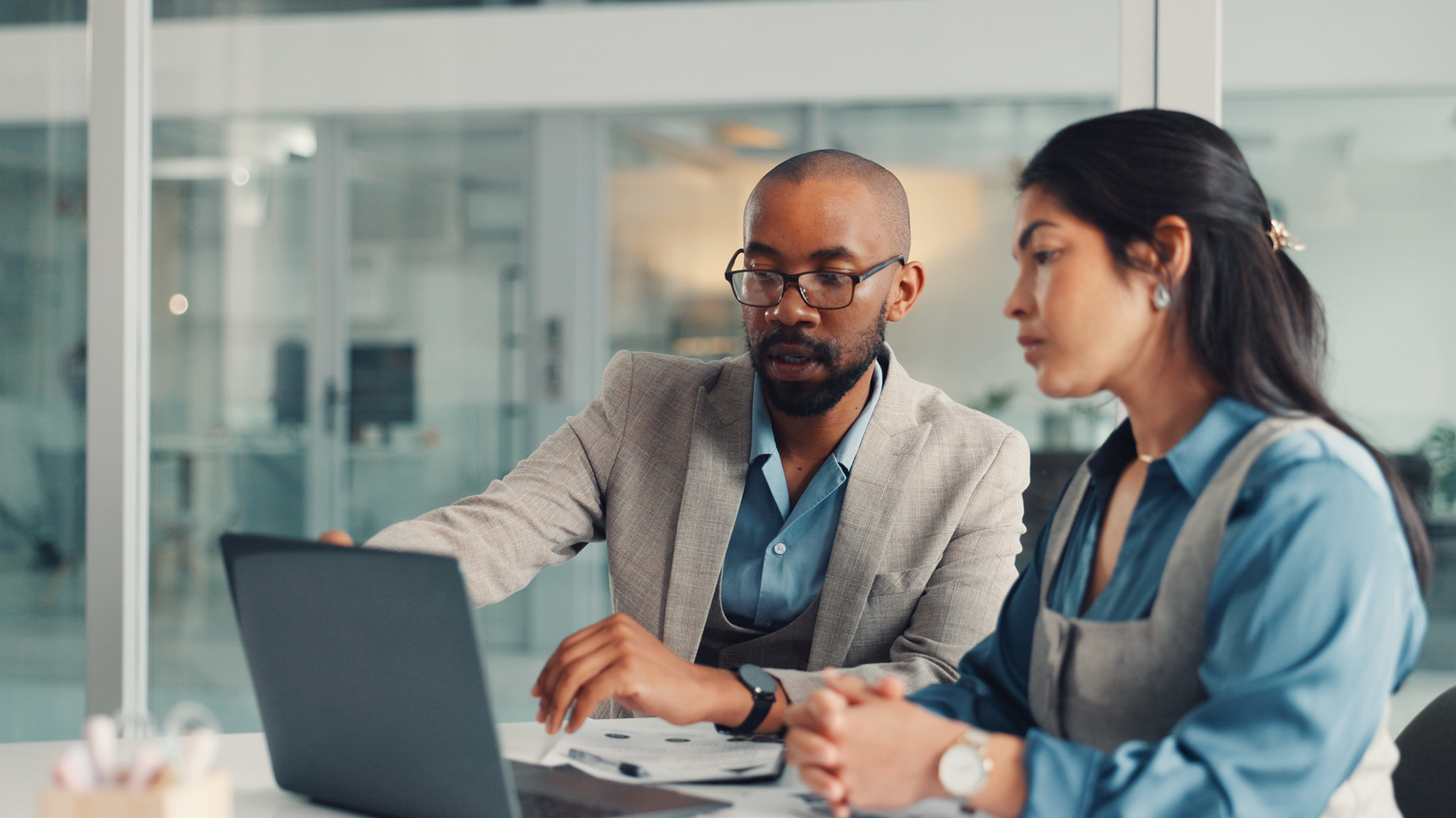 A financial advisor is sitting with a client and pointing to a laptop.